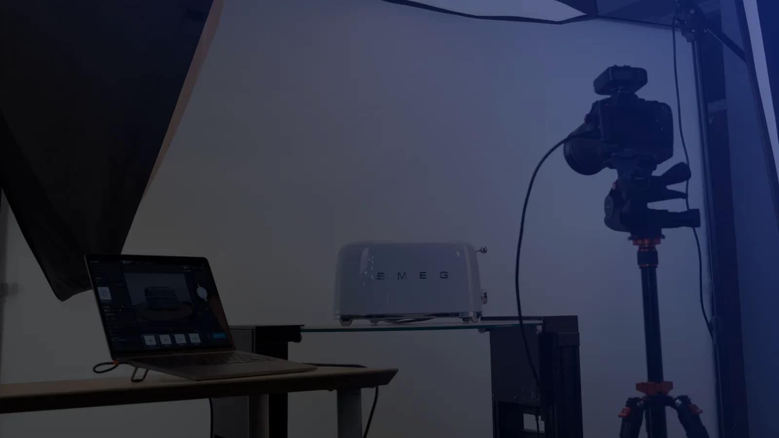 Set de fotografia de produto com tethering: um portátil com o software de captação junto a uma câmara em tripé e um produto sobre uma prateleira de vidro