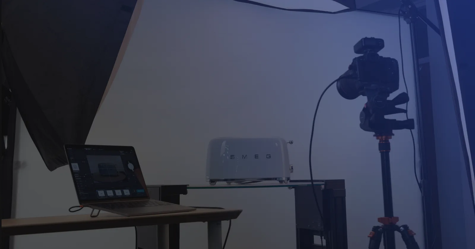 Set de fotografia de produto com tethering: um portátil com o software de captação junto a uma câmara em tripé e um produto sobre uma prateleira de vidro